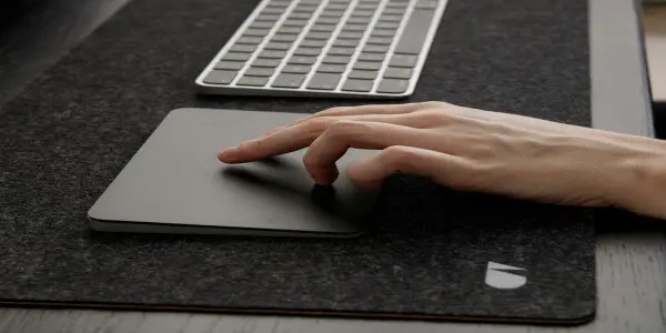 Apple Magic Trackpad noir à côté d'un MacBook Pro ouvert sur un bureau
